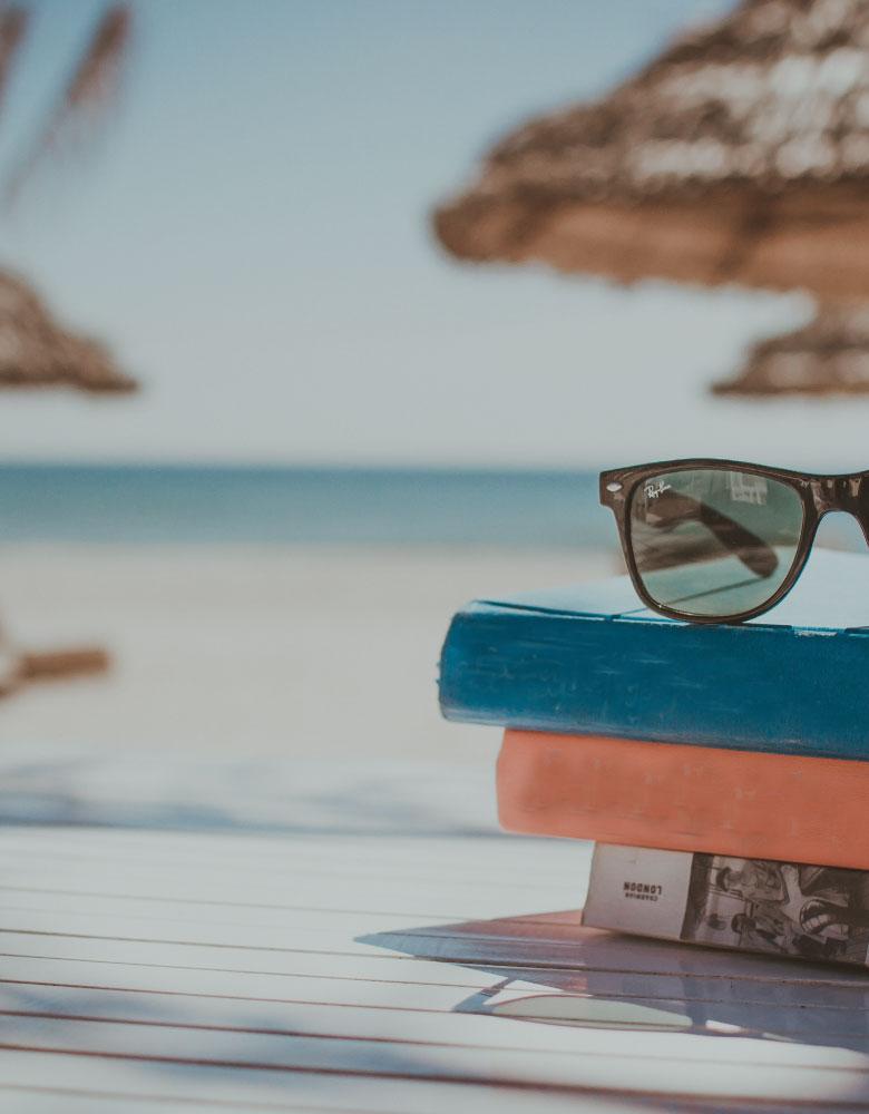 fotografia della spiaggia cattolica con dei libri e un paio di occhiali appoggiati sulla sabbia fine e dorata